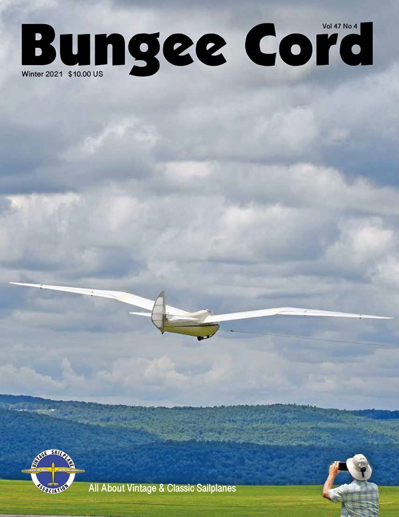A cover of Bungee Cord magazine featuring a white Minimoa glider being towed into a cloudy sky seen from behind. 